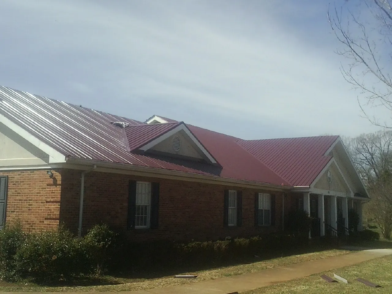 Red metal roof with gabled entries on a long brick building, from a Hail Damage Roof Repair job in Rocky Point