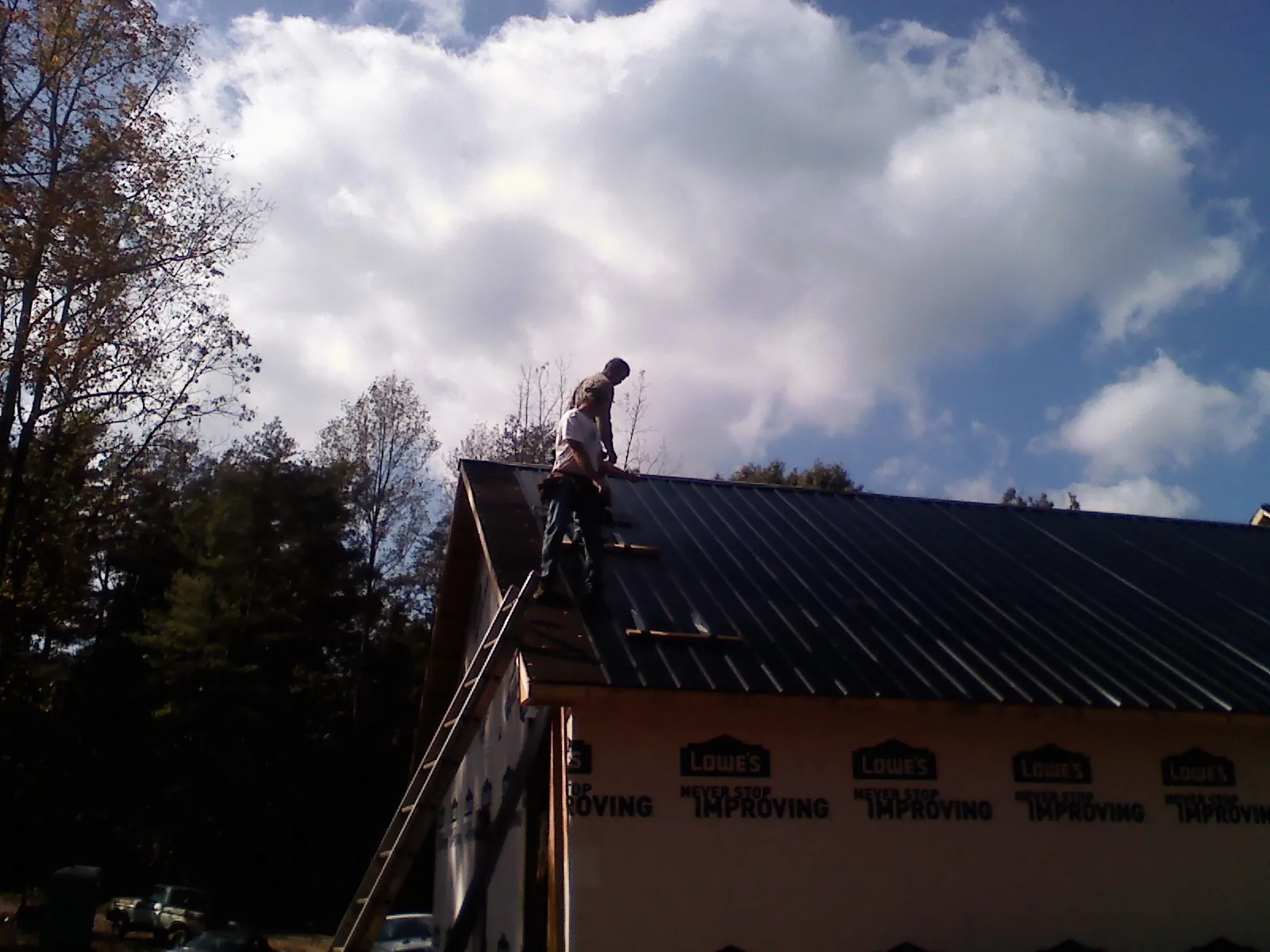 Roofer fastening dark metal panels high against a cloudy sky, from a Roof Inspection job in Rocky Point